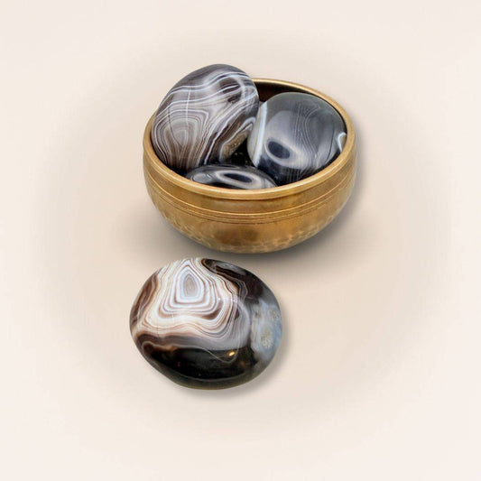 Collection of medium Sardonyx palm stones in a brass bowl, showcasing polished finishes and natural earthy patterns for crystal healing.