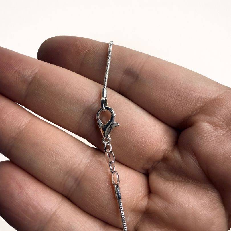 Lobster clasp detail of the Silver Snake Chain Necklace held in hand. Secure and adjustable closure for versatile jewelry styling.