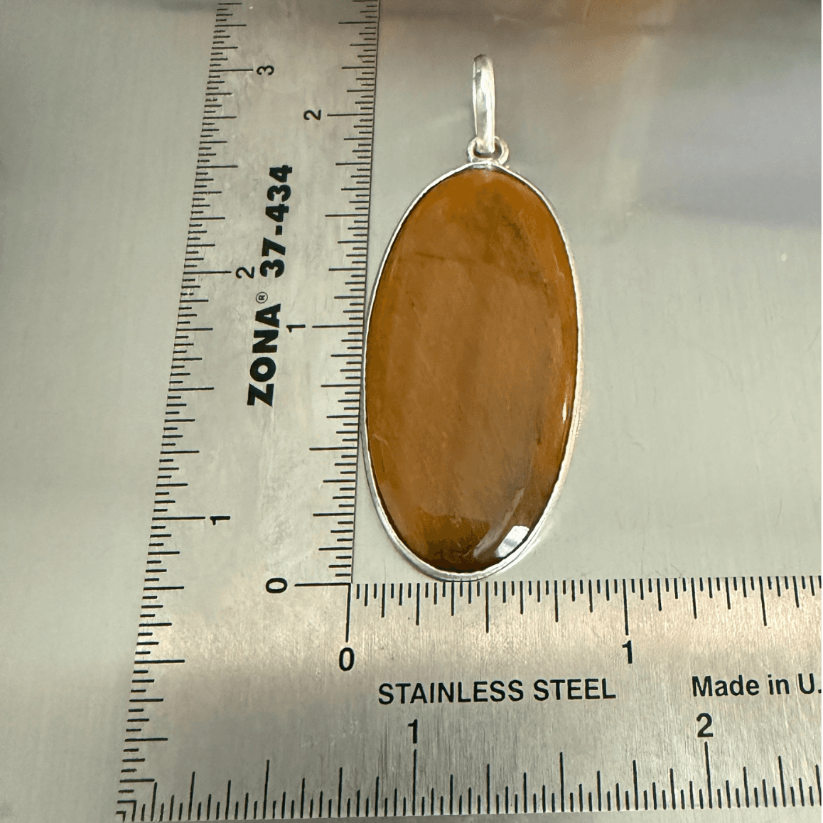 Tigers Eye Oval Pendant in sterling silver with warm golden-brown hues, shown next to a ruler for scale. Enhances courage, clarity, and protection.