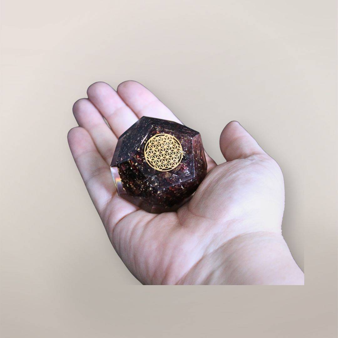 Two inch Garnet orgonite dodecahedron with golden Flower of Life symbol resting in a hand to show size and scale