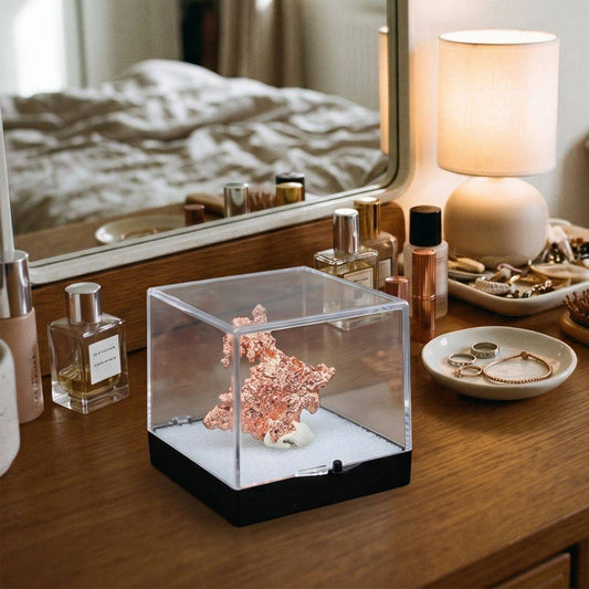 Sculptural native copper specimen from China displayed inside a clear protective perky box on a wooden vanity beside perfume bottles and jewelry.