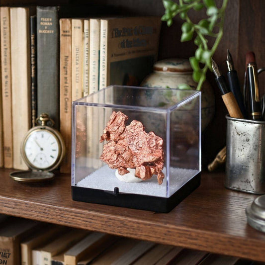 Native copper specimen from China displayed in a clear protective perky box on a wooden bookshelf beside vintage books, a pocket watch, and writing instruments.