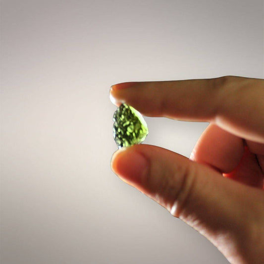 Backlit in-hand scale view of Czech Republic Moldavite showing its thumbnail size, tapered outline, and bright yellow-green transmitted color.