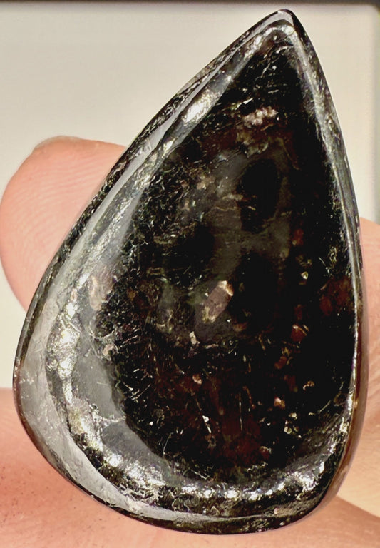 Close up view of 25ct Nuummite tear drop cabochon with golden flashes