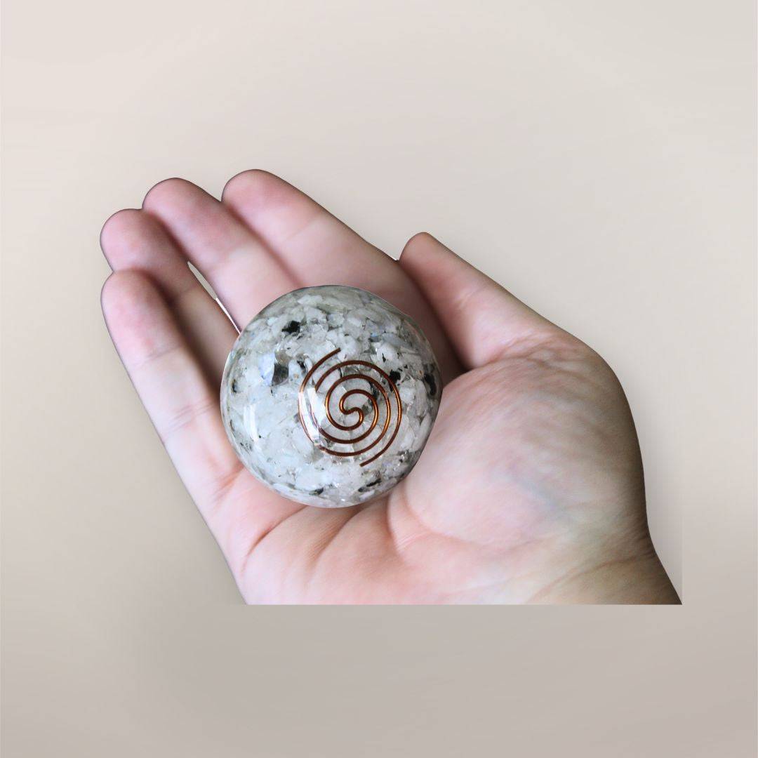 Two inch Rainbow Moonstone orgonite sphere with copper spiral resting in a hand to show size and scale