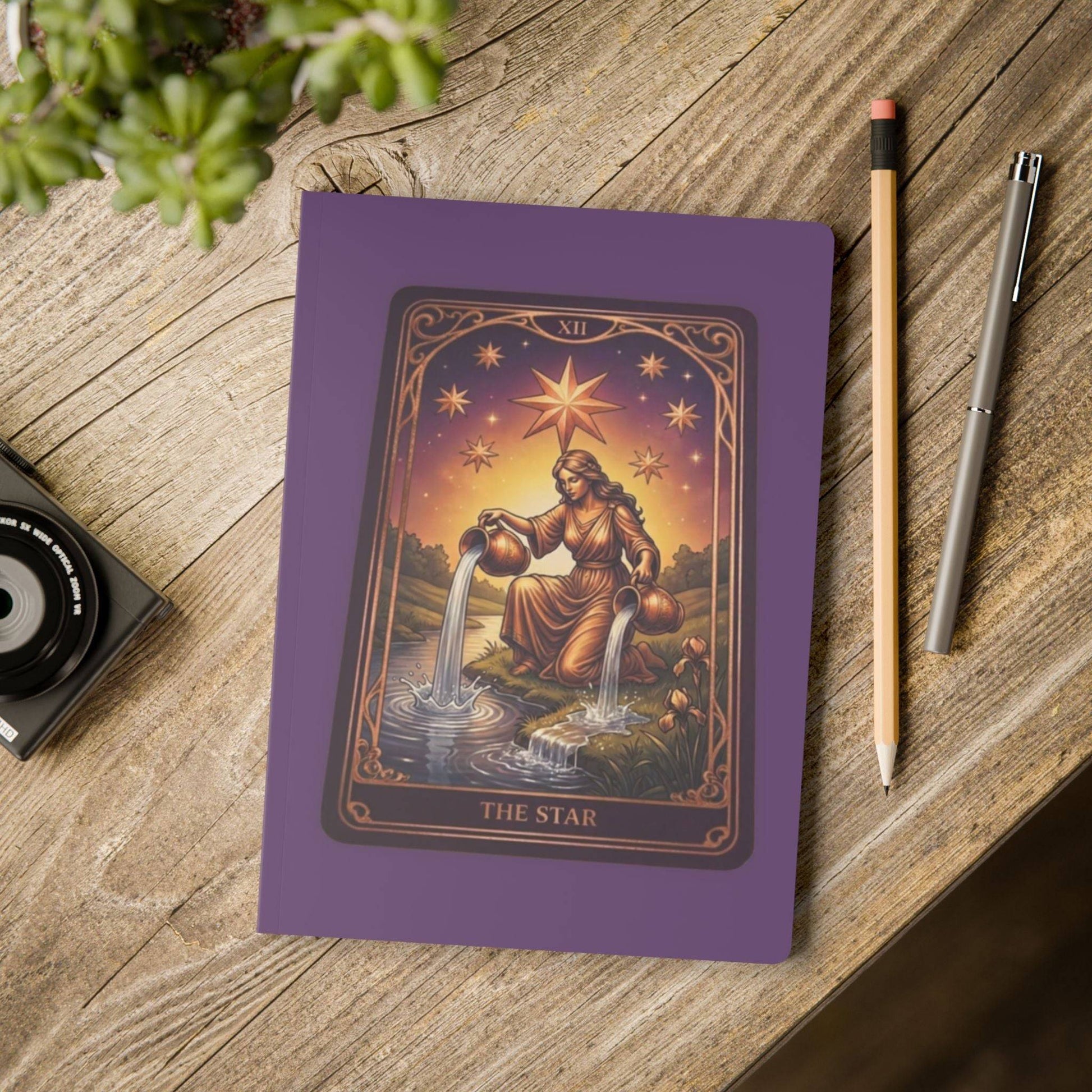The Star Tarot Softcover Journal placed on a rustic desk with pencil and camera, showcasing its artistic design for creative and spiritual use.