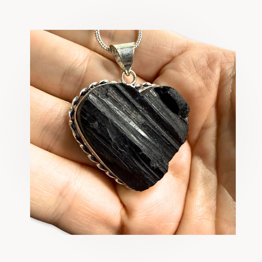 Hand holding Black Tourmaline Heart Pendant, displaying raw crystal texture and silver setting for grounding and energy shielding.