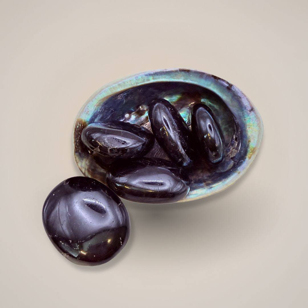 Black Tourmaline Palm Stone with iridescent sheen on a neutral background