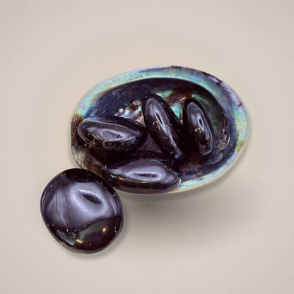 Black Tourmaline Palm Stone with iridescent sheen on a neutral background
