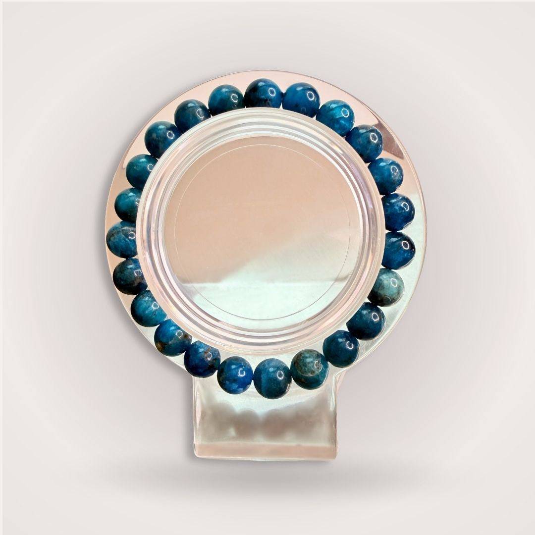 Gemmy Blue Apatite 8mm Beaded Bracelet displayed on a clear stand, showcasing its vibrant ocean-blue clarity and motivational energy.