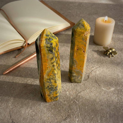 Two Bumblebee Jasper Towers on a stone surface with a candle and journal, symbolizing creativity, confidence, and chakra alignment in a calming setup.