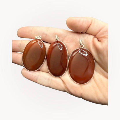 Three Carnelian Statement Pendants displayed in hand, each with unique red-orange tones, intuitively selected to enhance vitality and confidence.
