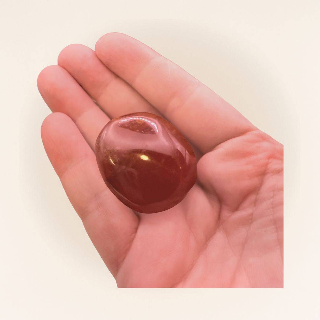 Single Carnelian Tumbled Stone held in hand, showcasing its polished surface and vibrant color for confidence and creativity boosting.