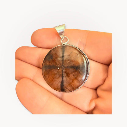 Close-up of a round Chiastolite Cross Stone Pendant held in hand, emphasizing its polished finish and natural cross pattern for spiritual protection.