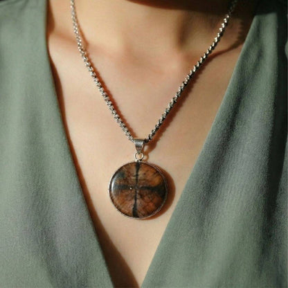Round Chiastolite Cross Stone Pendant worn on a silver chain, showcasing its natural cross pattern and spiritual symbolism for balance and protection.