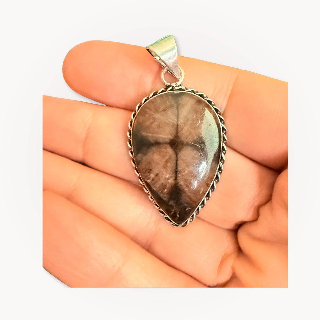 Close-up of teardrop Chiastolite Cross Stone Pendant held in hand, emphasizing its unique cross design and polished finish.