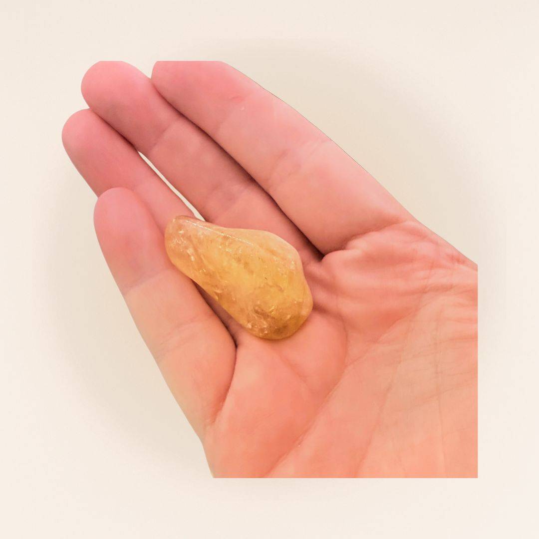 Hand holding a Citrine Tumbled Stone from Brazil, showcasing its size and golden clarity for use in crystal healing and empowerment.