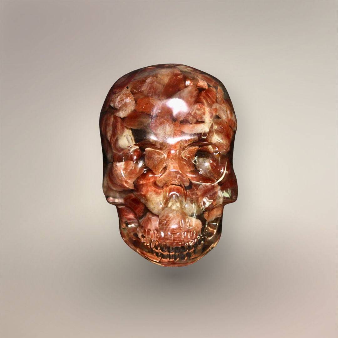 Front view of Confetti Sunstone skull orgonite with densely packed peach, copper-red, cream, and translucent stone chips in clear resin.