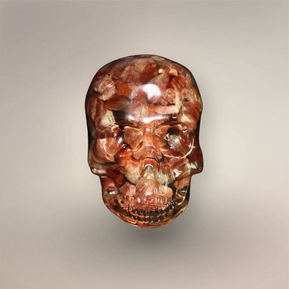 Front view of Confetti Sunstone skull orgonite with densely packed peach, copper-red, cream, and translucent stone chips in clear resin.