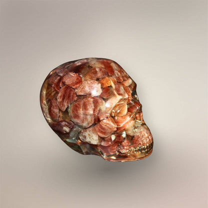 Three-quarter side view of the Confetti Sunstone skull orgonite showing its rounded cranium, layered stone chips, clear resin, and carved jaw detail.