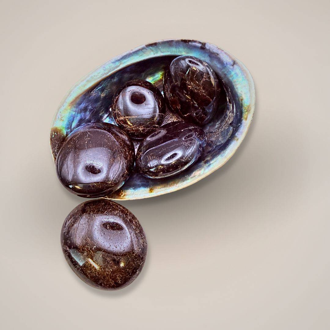 Garnet gemstone in shell dish with beads and hand for size comparison