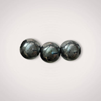 Close-up of three polished 12mm Hematite beads from the Hematite 12mm Beaded Bracelet - Grounding & Stable Protective, showcasing natural shine.