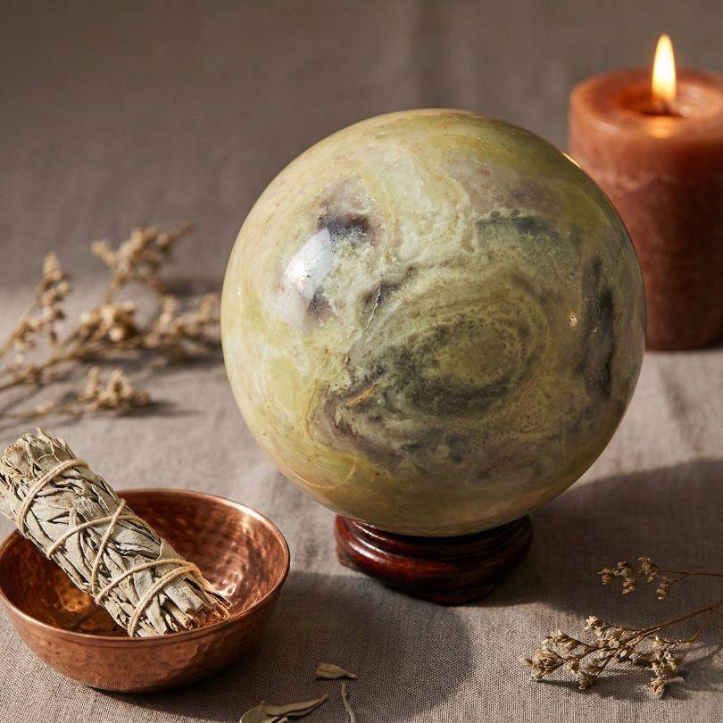 Heart Chakra Healing Infinite Stone Sphere from Peru displayed with sage and candle, perfect for meditation and spiritual rituals.