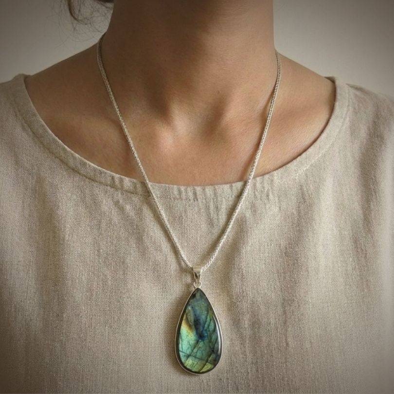 Labradorite Statement Pendant worn on model, showcasing its teardrop shape and iridescent blue-green hues for spiritual protection.