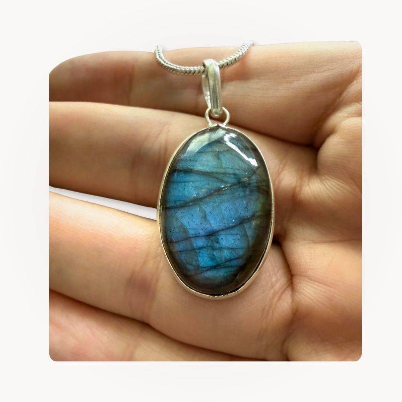 Hand holding Labradorite Classic Pendant with vivid blue sheen, highlighting its protective and intuitive properties in jewelry design.