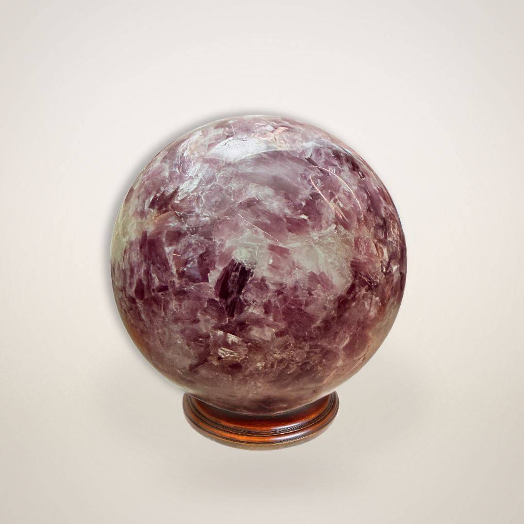 Lepidolite Sphere 64mm displayed on wooden stand, showcasing polished surface and soothing crystal patterns for stress relief and decor.