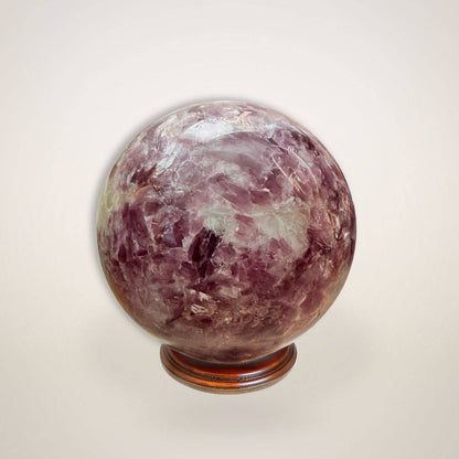 Lepidolite Sphere 64mm displayed on wooden stand, showcasing polished surface and soothing crystal patterns for stress relief and decor.