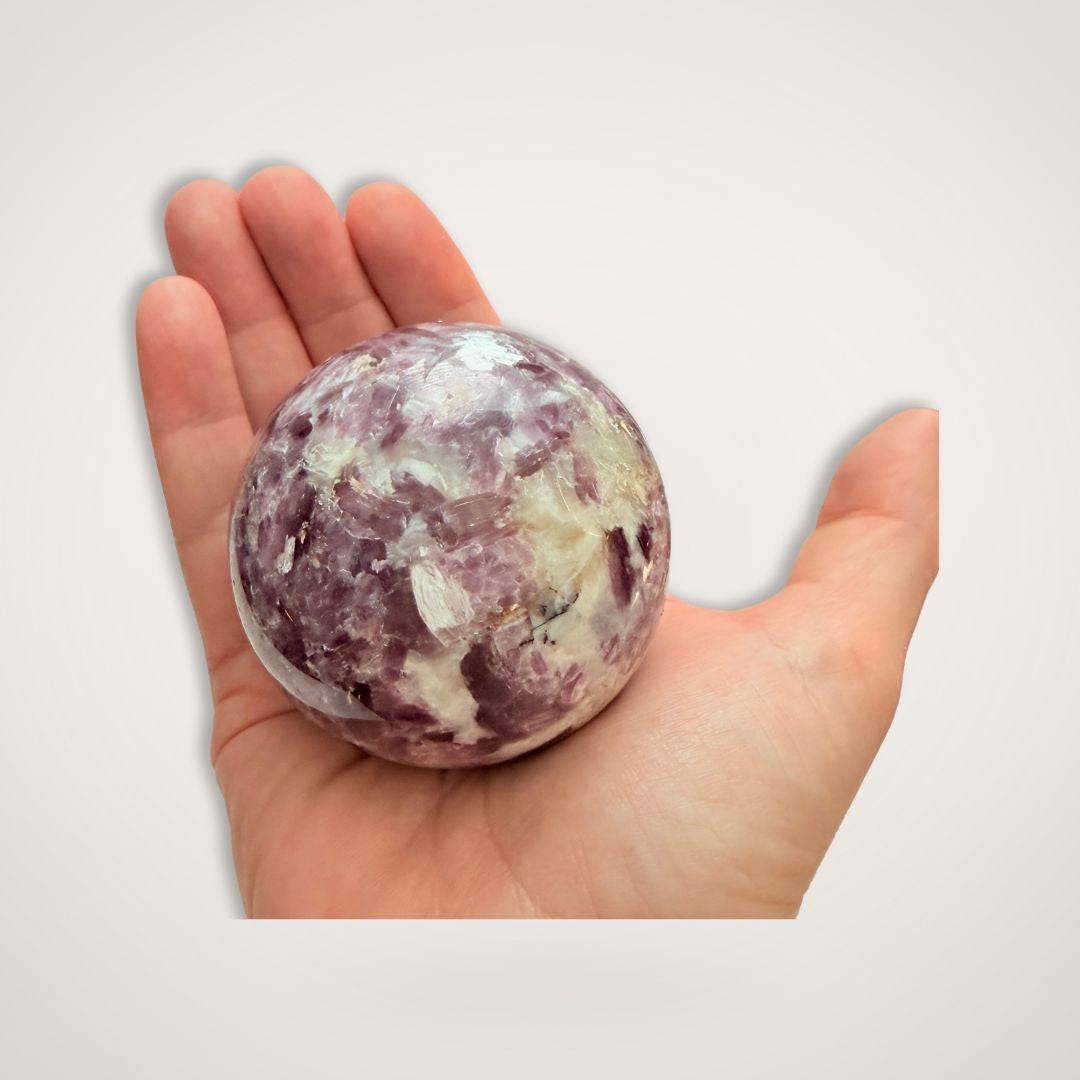 Polished Lepidolite Sphere 64mm shown in hand, highlighting its calming purple tones and compact size for emotional balance rituals.
