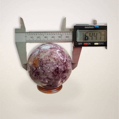 Close-up of Lepidolite Sphere 64mm measured with caliper, confirming size and quality for collectors and crystal healing enthusiasts.