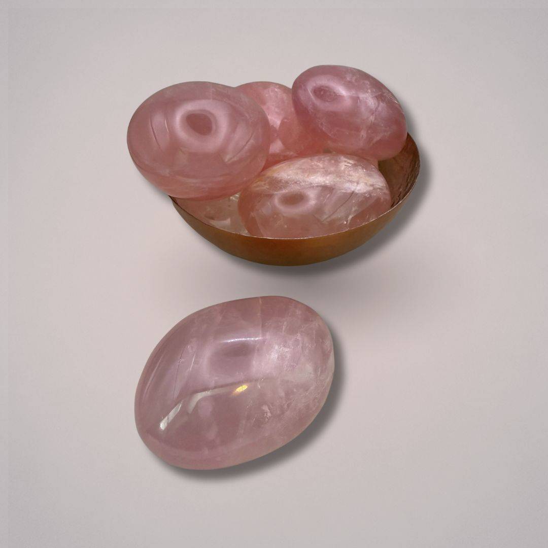 Group of large polished rose quartz palm stones from Madagascar, one displayed outside a brass bowl for crystal healing and decor use.