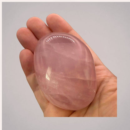 Hand holding a large, polished rose quartz palm stone from Madagascar, showcasing its smooth texture and soft pink hue.
