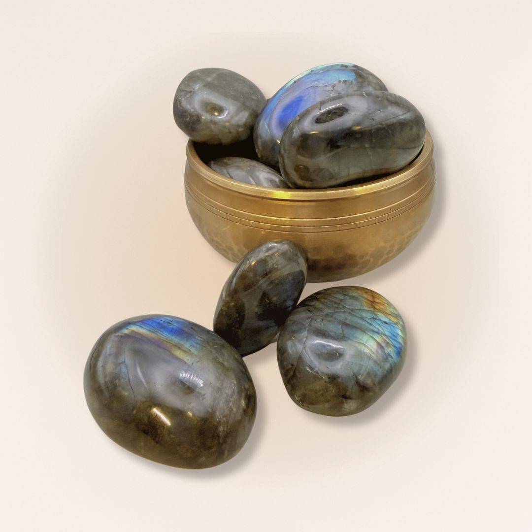 Group of polished medium Labradorite palm stones in and around a brass bowl, showcasing iridescent flashes for spiritual insight and protection.