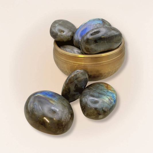 Group of polished medium Labradorite palm stones in and around a brass bowl, showcasing iridescent flashes for spiritual insight and protection.