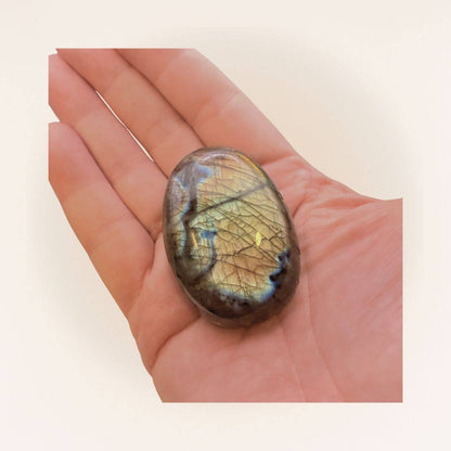 Polished medium Labradorite palm stone with golden-blue flash resting on a hand, perfect for intuitive practices and energy shielding.