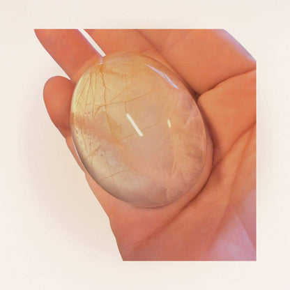 Medium Peach Moonstone Palm Stone held in hand, showcasing its smooth finish and warm tones for intuitive and calming energy work.