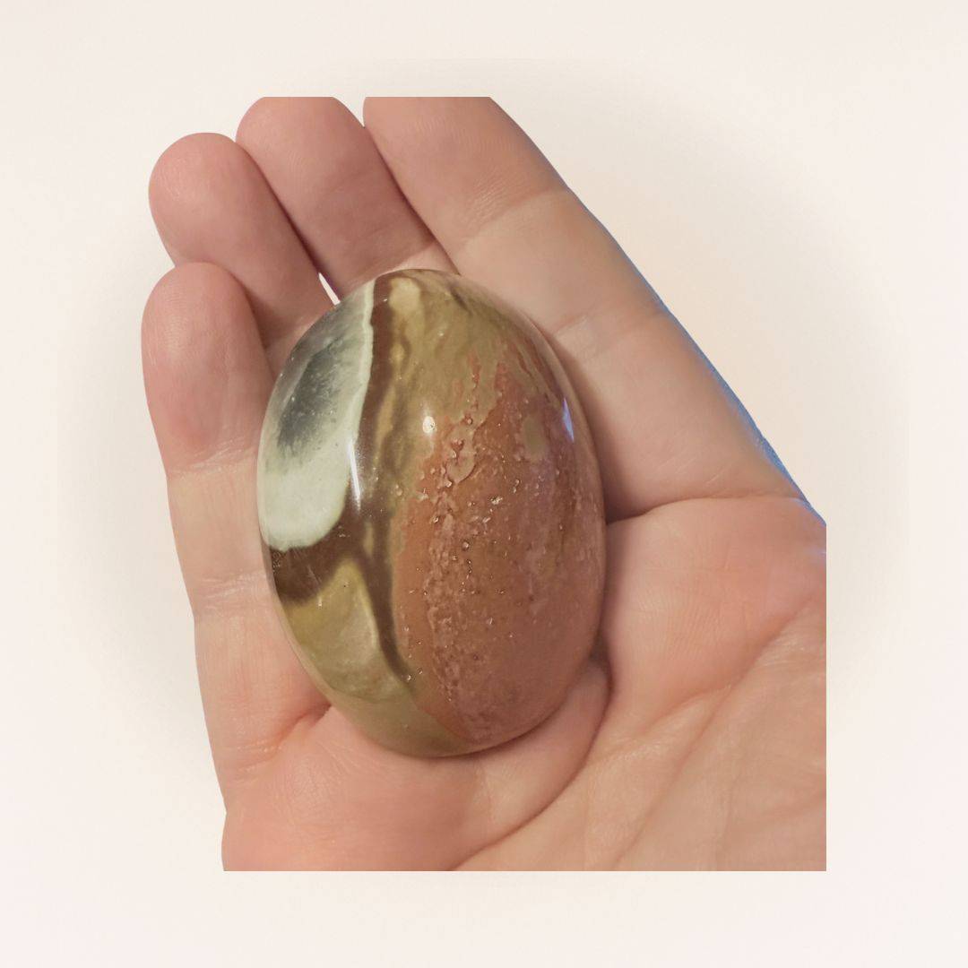 Hand holding a medium Polychrome Jasper palm stone, highlighting its smooth texture and multicolored natural patterns for crystal healing.