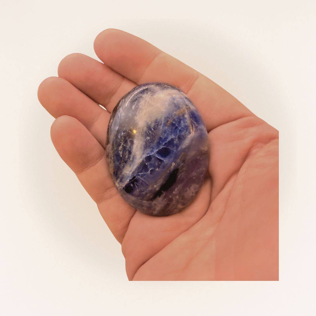 Polished medium Sodalite palm stone resting in a hand, showcasing its deep blue tones for clarity, communication, and peaceful energy.