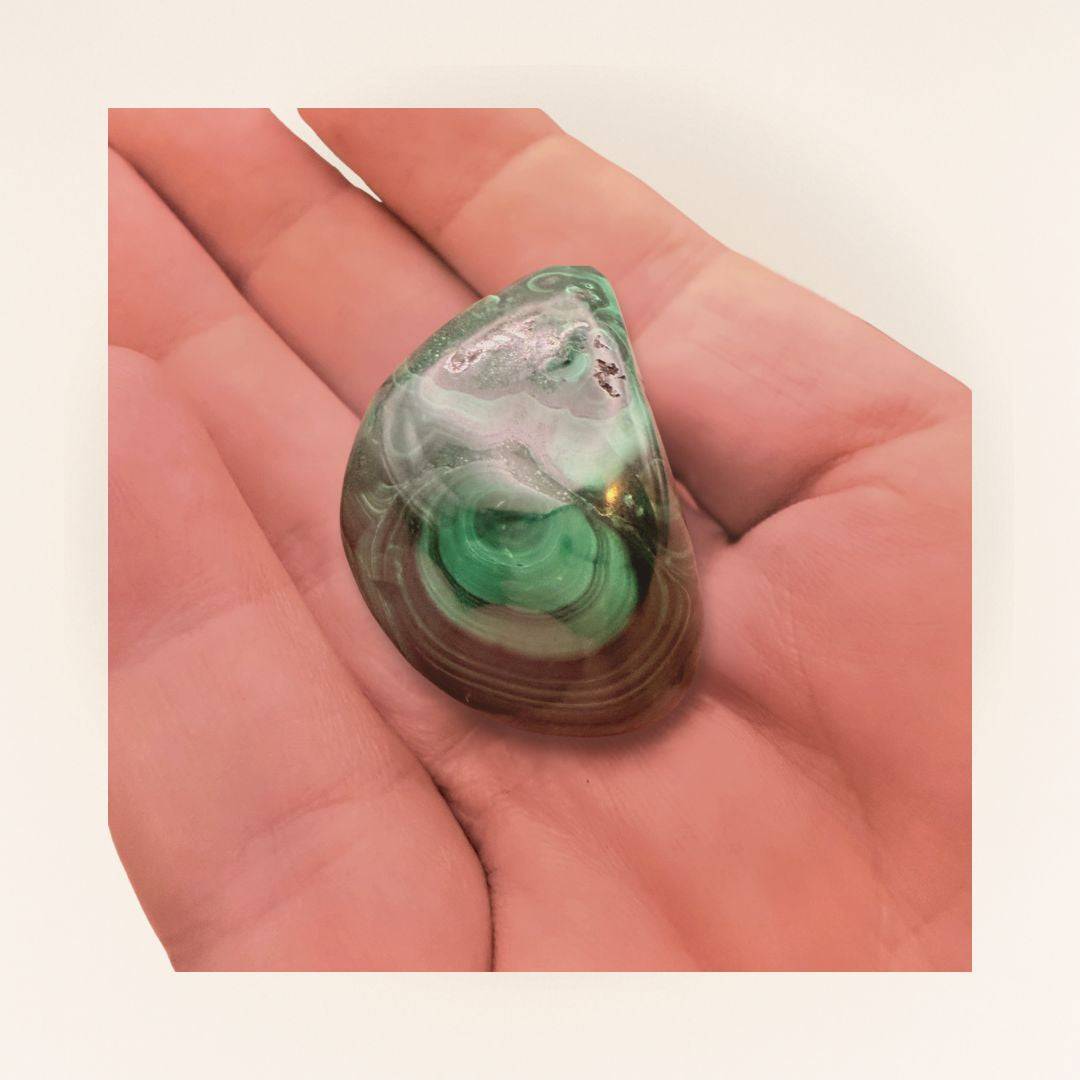 Single Malachite Tumbled Stone resting on a hand, highlighting its unique patterns for chakra healing and spiritual balance.