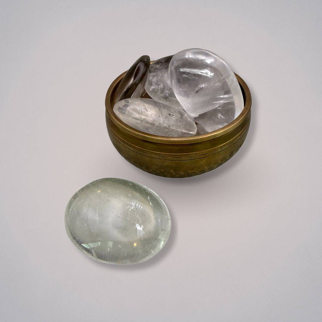 Polished Water Clear Quartz Palm Stones from Brazil in a brass bowl with one stone placed outside, collectible gemstones by Mystic Parcel.