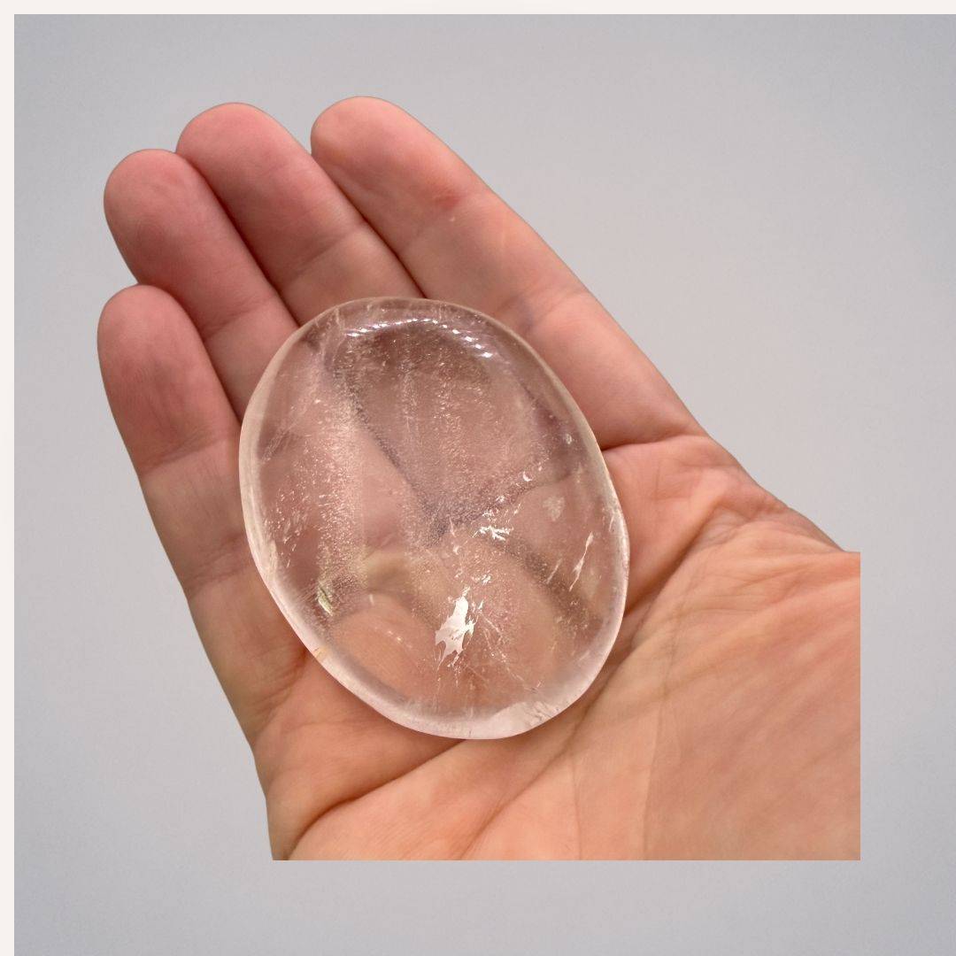Hand holding a polished Water Clear Quartz Palm Stone from Brazil, medium size, showcasing its clarity and smooth finish for energy cleansing.