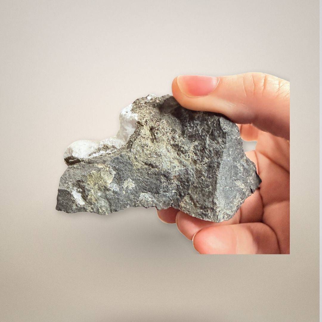 Hand holding Natrolite micro-needles specimen showing scale and texture of basalt matrix with white zeolite crystal formation.