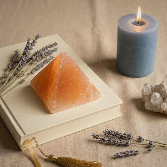 Orange Selenite Pyramid placed on a book with lavender, candle, and crystals, perfect for energy balancing and spiritual home decor.