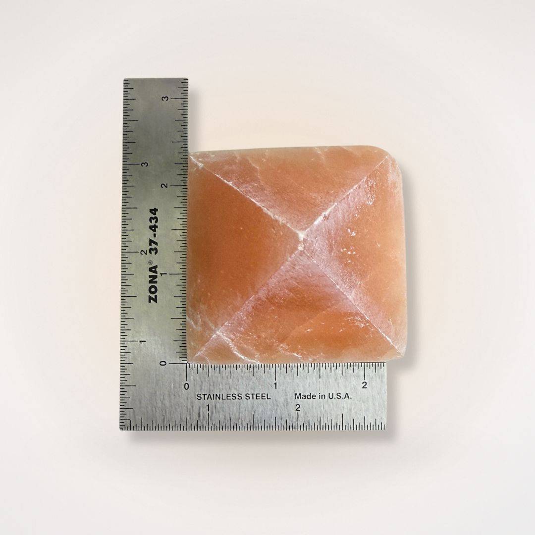 Orange Selenite Pyramid measured with ruler, approximately 2.5 inches wide, perfect for energy balancing and decorative use.