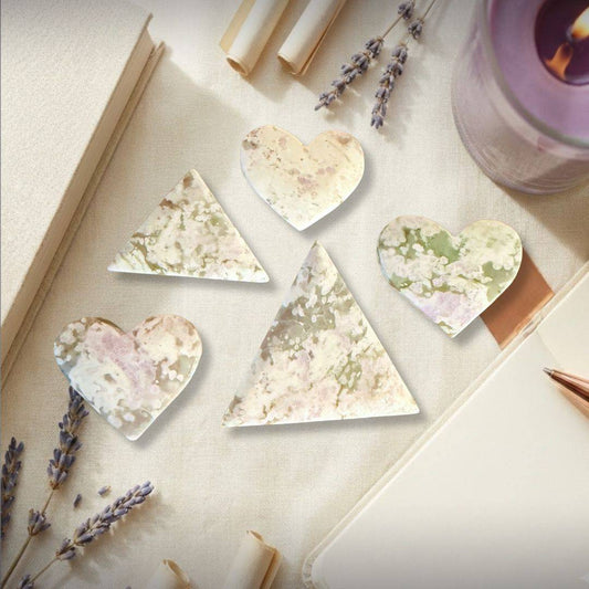 Peace Jade palm stones in heart and triangle shapes, made of lavender serpentine and stichtite, displayed with lavender and candles.
