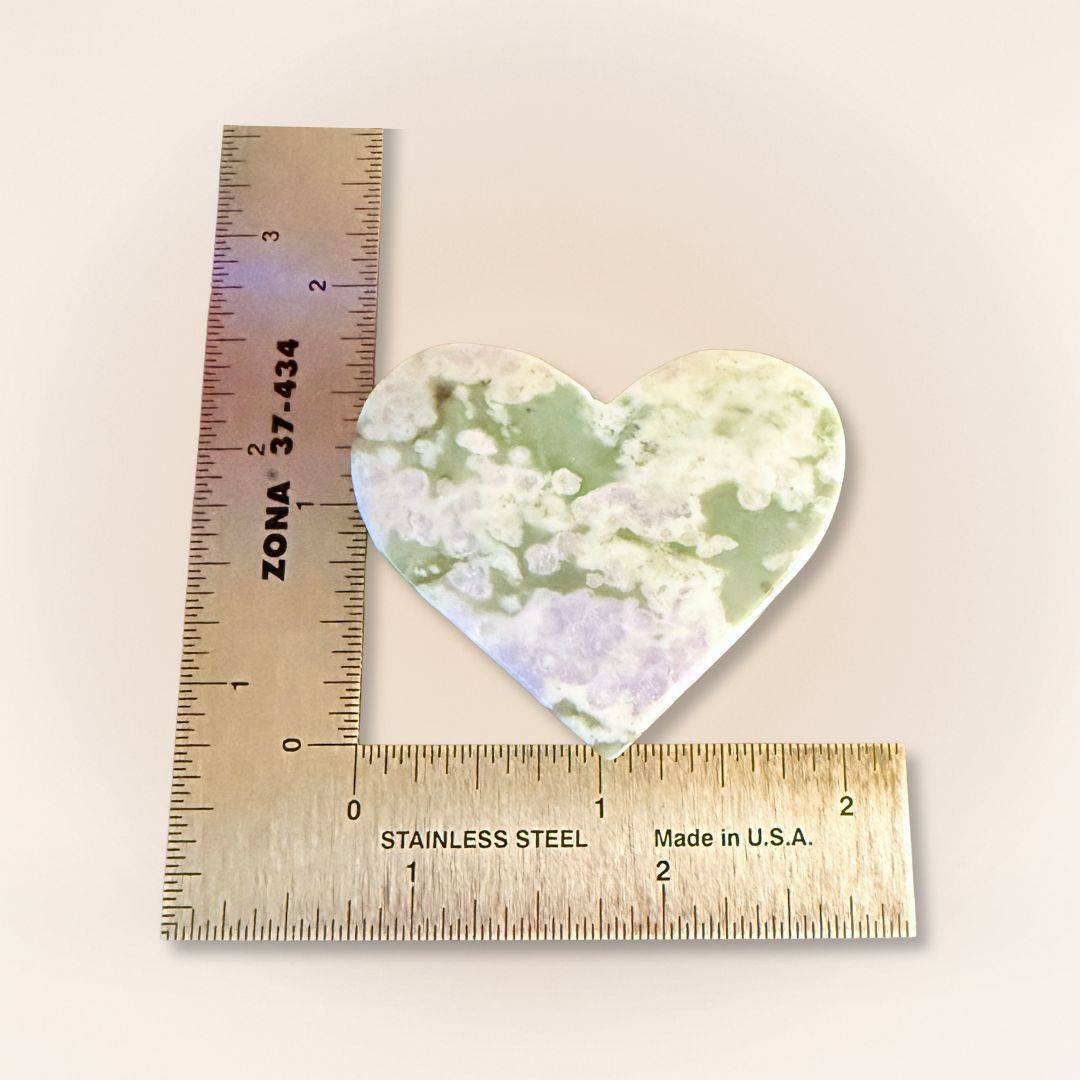 Peace Jade heart palm stone beside ruler for scale, showcasing lavender and green serpentine with stichtite inclusions.