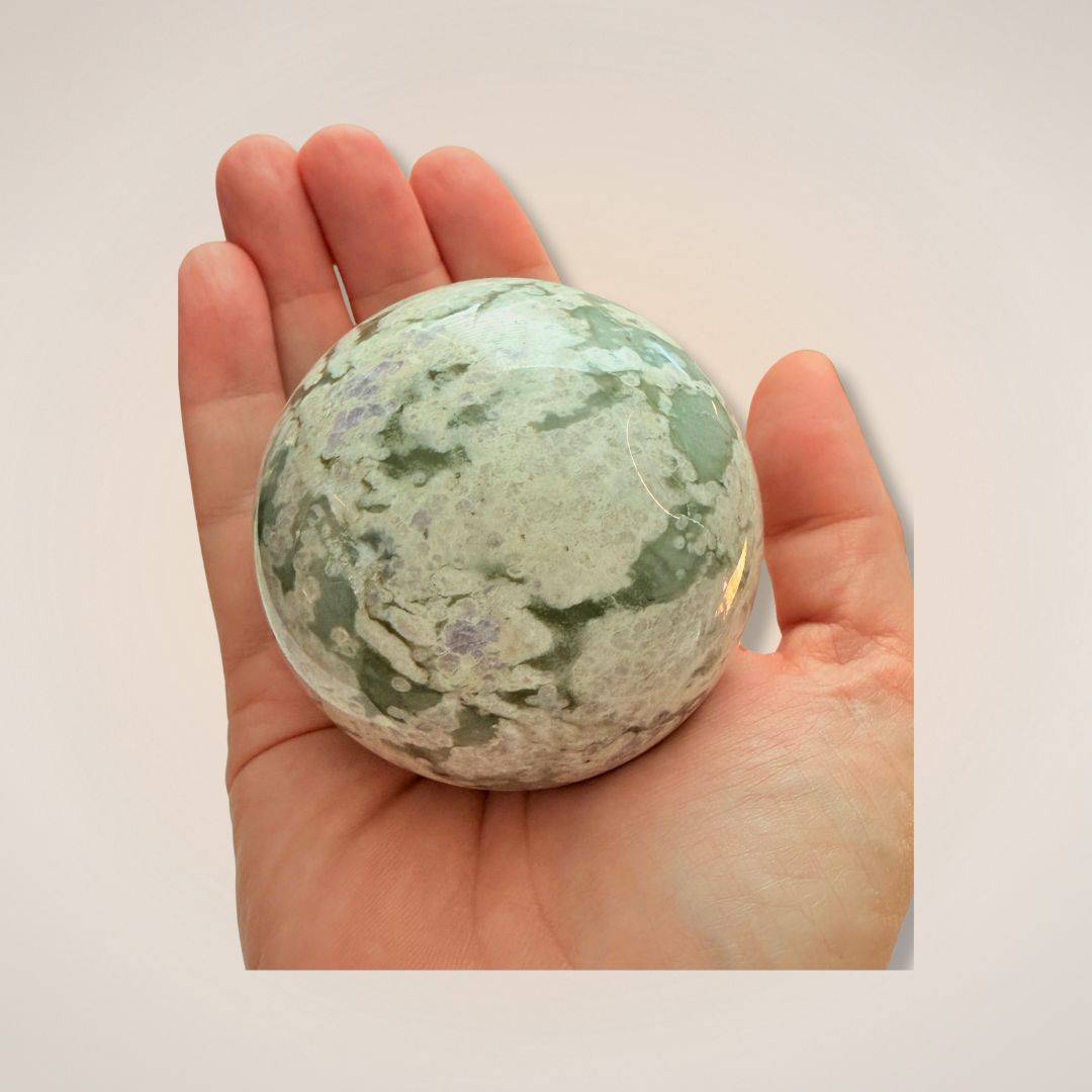 Peace Jade Sphere 66mm shown in hand for scale, showcasing its smooth texture and calming green-white coloration for inner peace.
